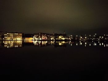 Illuminated city by river against clear sky at night