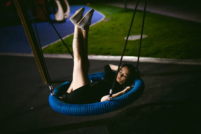 Young woman resting on swing in park at night