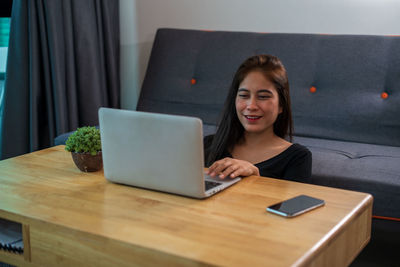 Young woman using phone while sitting on table