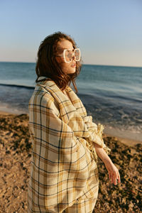 Young woman standing at beach against sky