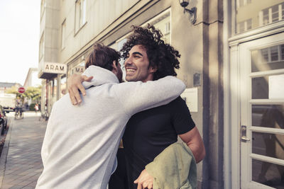 Cheerful male friends hugging each other outside cafe