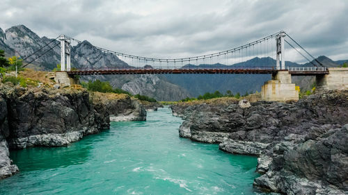 Suspension bridge over a mountain river. mountain turquoise river, rocky shores. drone shooting.