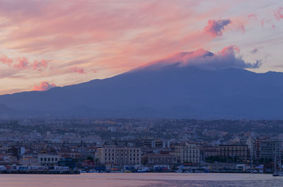 Cityscape of catania from harbor and etna on the background.