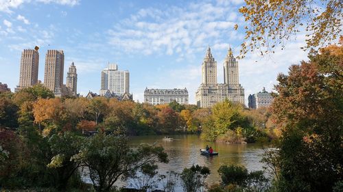 Trees and buildings by river against sky