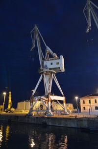 Cranes at harbor against sky at night