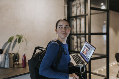 Businesswoman with laptop and backpack leaving from creative office