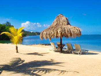 Deck chairs., palapa on beach against blue sky