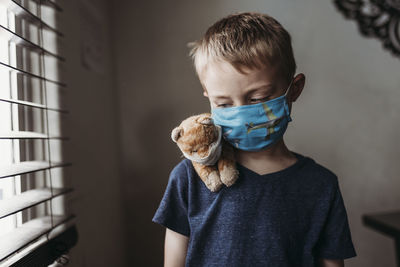 Close up of young school aged boy with mask on with stuffed animal negative space