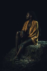 Black woman under a night sky semi with just a sweater sitted on a rock