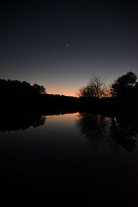 Reflection of silhouette trees in lake against sky at night