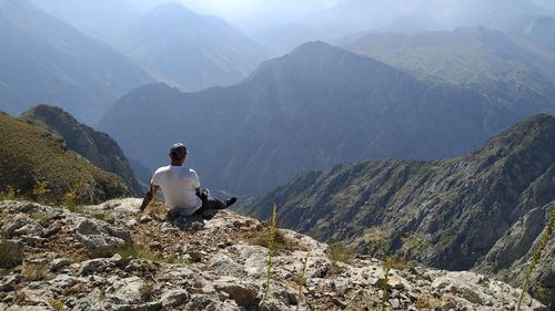 Rear view of man sitting on rock looking at mountains
