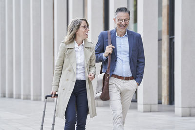 Happy mature businesswoman walking with colleague on footpath