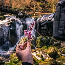 Midsection of man photographing plant against waterfall