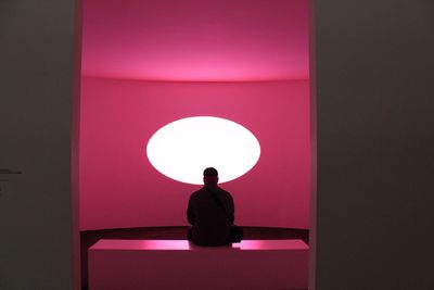 Rear view of man sitting against illuminated wall