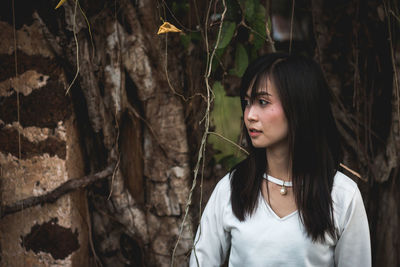 Thoughtful young woman standing against tree in forest