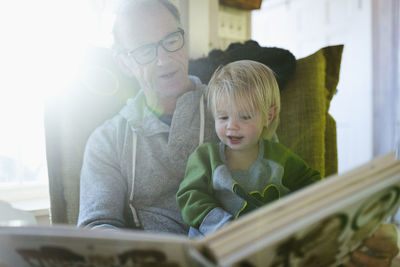 Low angle view of grandfather with granddaughter reading book while sitting on chair at home