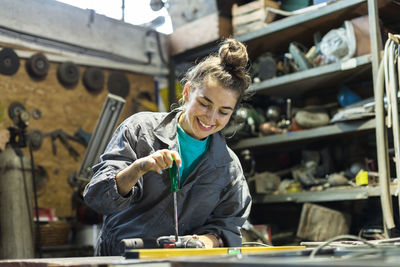Low angle view of smiling mid adult woman working on desk in workshop