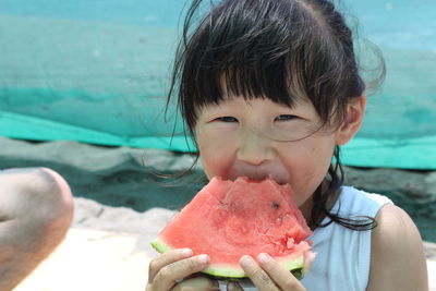 Portrait of girl eating watermelon slice while sitting at beach