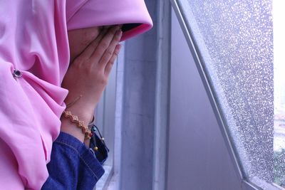 Side view of upset woman standing at window during rain