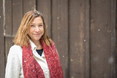 Portrait of smiling woman wearing warm clothing against wooden wall during winter