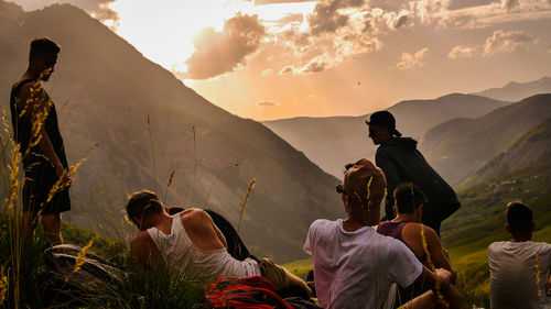 People sitting on land by mountain against sky during sunset