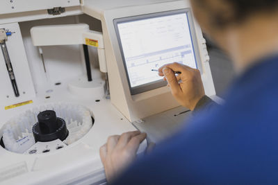 Back view of crop male doctor in uniform looking at monitor near specimens in chemistry test analysis machine