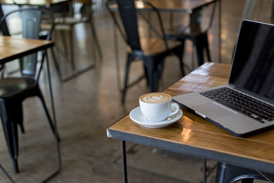 Close-up of coffee cup by laptop on table in cafe