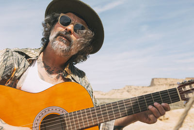 Free traveling young hipster man playing the guitar while traveling in the mountains. country music