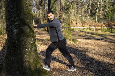 Runner is leaning against an oak tree and is stretching. 