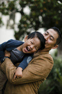 Low angle view of father carrying happy son while standing against trees in balboa park