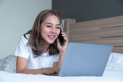 Smiling young woman using mobile phone on bed