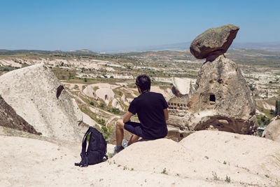 Guy in a black t-shirt sit back on a rock with a backpack spreading his hands to the sides