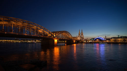 Illuminated bridge over river against sky at night