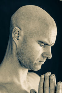 Close-up of shaved head man with hands clasped against black background