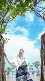 Woman standing by tree trunk against sky