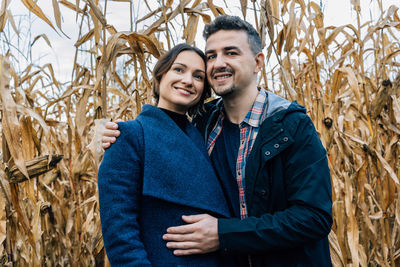 Happy couple in love stands in autumn near cornfield. man in shirt and jacket hugs woman in coat