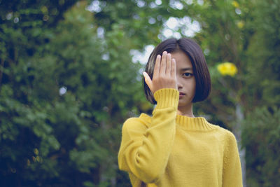 Portrait of teenage girl covering eye with hand against trees