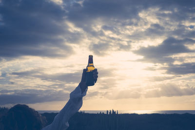 Cropped hand holding bottle against sky