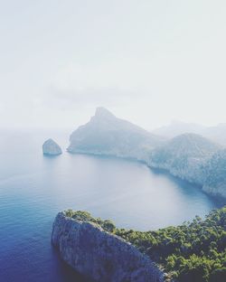 Scenic view of mountains by sea against clear sky during foggy weather