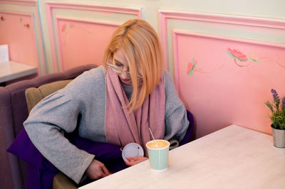 Young attractive blonde girl in cafe drinks coffee from a paper cup and relaxes