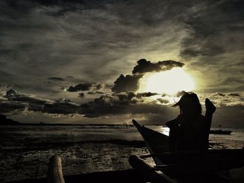 Silhouette woman sitting on beach against sky during sunset