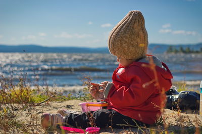 Side view of baby girl playing with sand while sitting on beach against blue sky