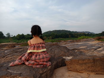 Rear view of woman sitting on rock against sky