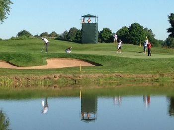 View of people on grassy field by lake