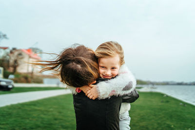 Rear view of mother embracing daughter on field