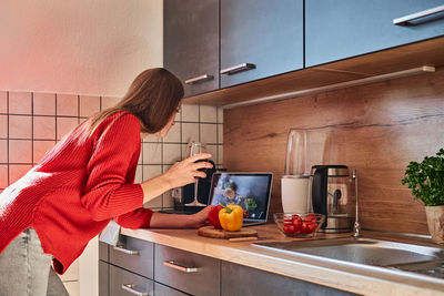 A young woman prepares a salad in the kitchen online and drinks red wine. cooking courses online