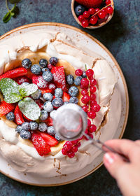 Cropped hand of woman sprinkling powdered sugar in bowl on table