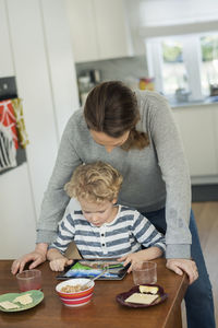 Mother and son using digital tablet at dining table in living room