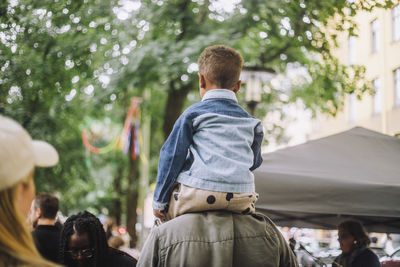 Rear view of man carrying son on shoulder at flea market