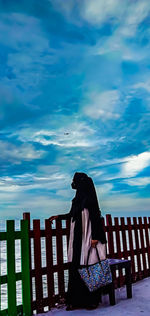 Side view of woman standing on bench against sky